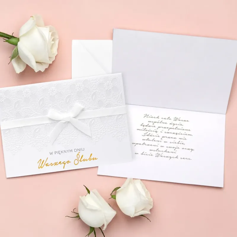 Jasny karnet z napisem „W pięknym dniu Waszego Ślubu”, białą kokardą, koronkowym tłoczeniem oraz białą kopertą