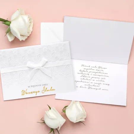 Jasny karnet z napisem „W pięknym dniu Waszego Ślubu”, białą kokardą, koronkowym tłoczeniem oraz białą kopertą