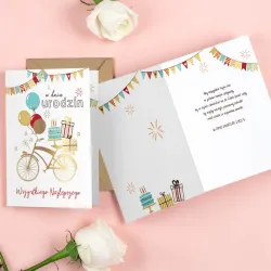 Karnet urodzinowy z rowerem, balonami, prezentami i ciemnozłotą kopertą.