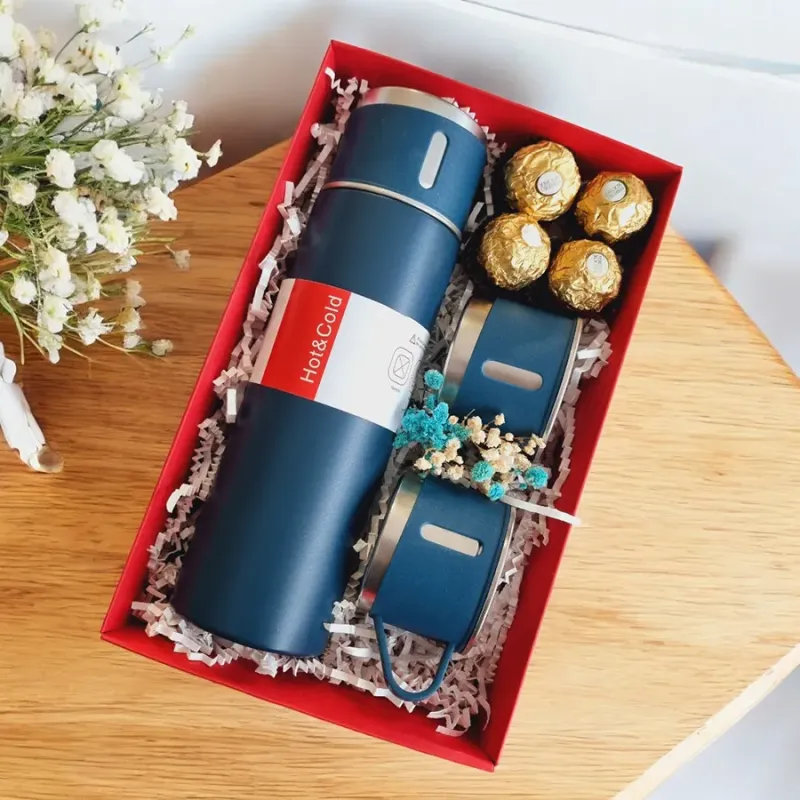 Otwarte czerwone pudełko z kubkiem termicznym i słodkościami ułożonymi obok siebie