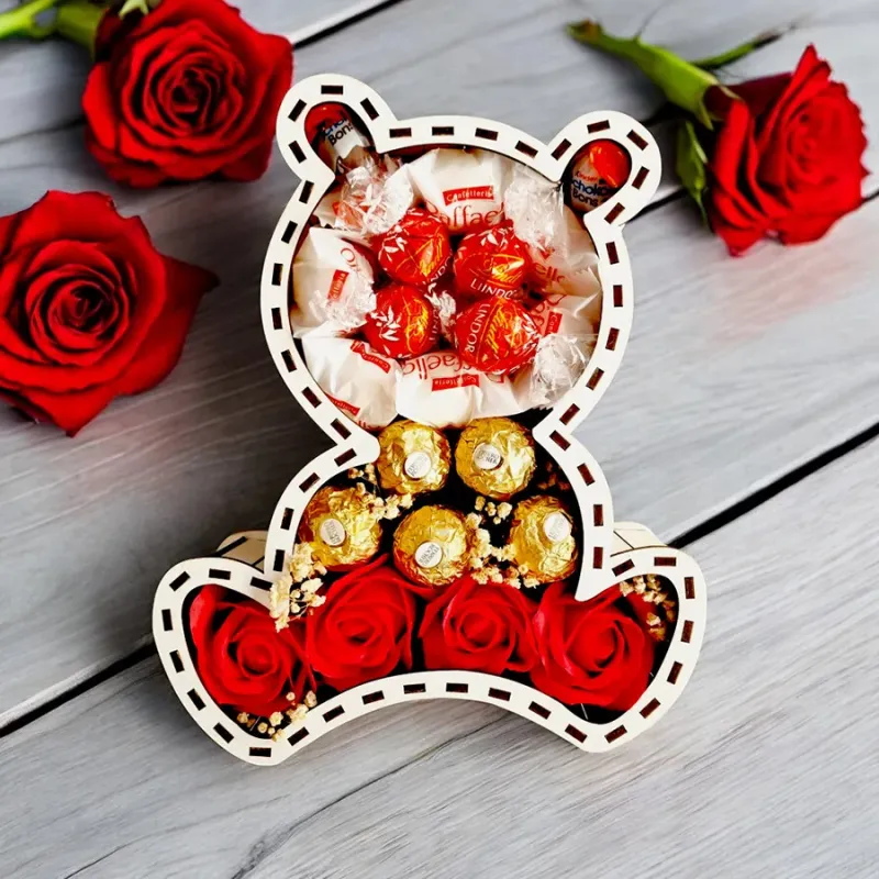 Otworzone pudełko w kształcie misia z czerwonym sercem, w środku pralinki i czekoladki