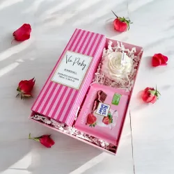 Wnętrze różowego pudełka ze świecą w kształcie piwonii, patyczkami zapachowymi i czekoladą