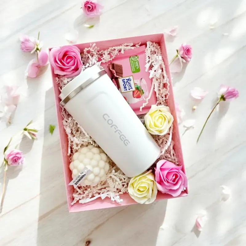 Wnętrze różowego pudełka z białym termosem, świecą bąbelkową kulą, różami mydlanymi i czekoladą