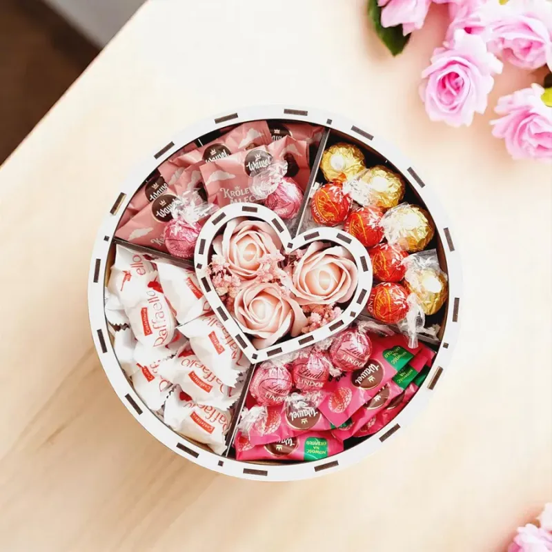 Wnętrze białego okrągłego pudełka z centralnym sercem, słodyczami oraz dekoracją z gipsówki i róż