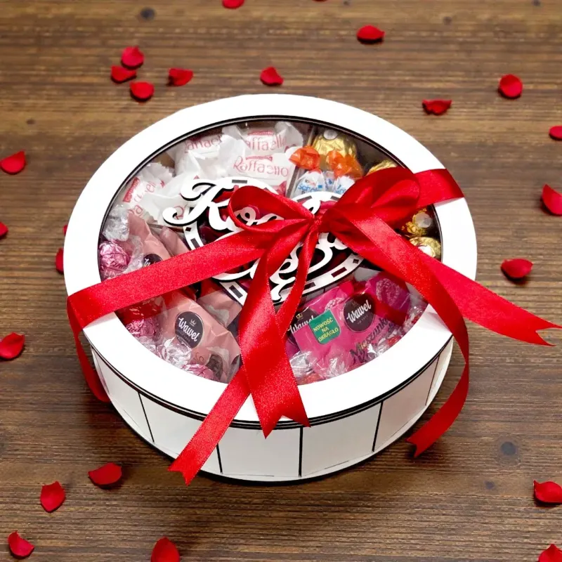 Białe okrągłe pudełko przewiązane czerwoną wstążką z dekoracyjną kokardą