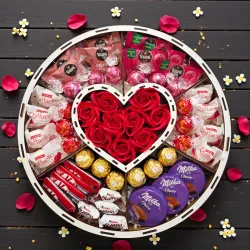 Wnętrze dużego białego okrągłego pudełka z centralnym sercem, czerwonymi różami mydlanymi i mixem słodyczy w przegródkach