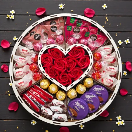 Wnętrze dużego białego okrągłego pudełka z centralnym sercem, czerwonymi różami mydlanymi i mixem słodyczy w przegródkach