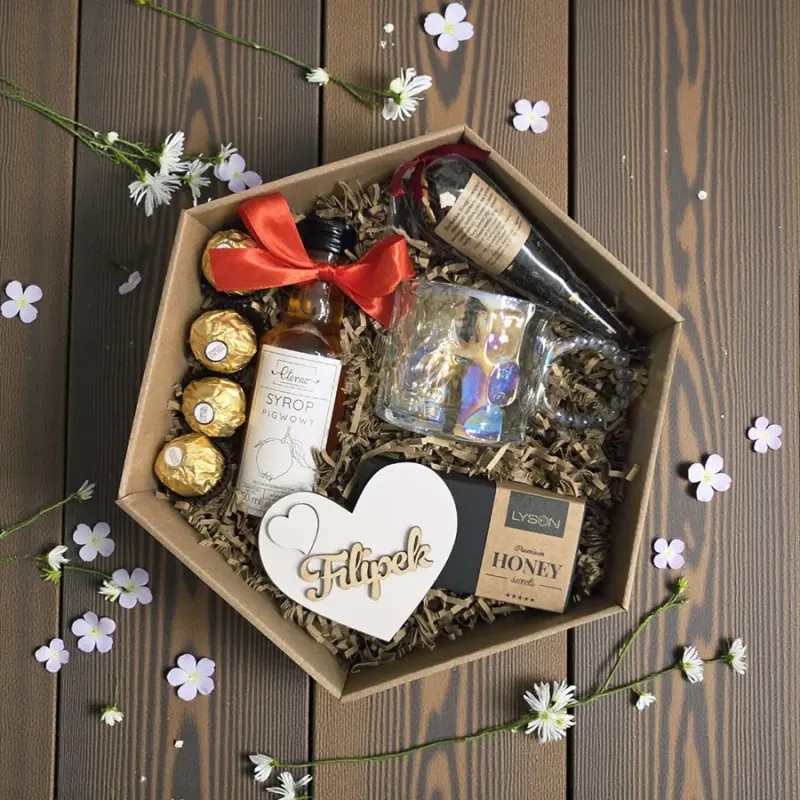 Wnętrze sześciokątnego brązowego pudełka z kubkiem, syropem, herbatką, miodową krówką i pralinkami